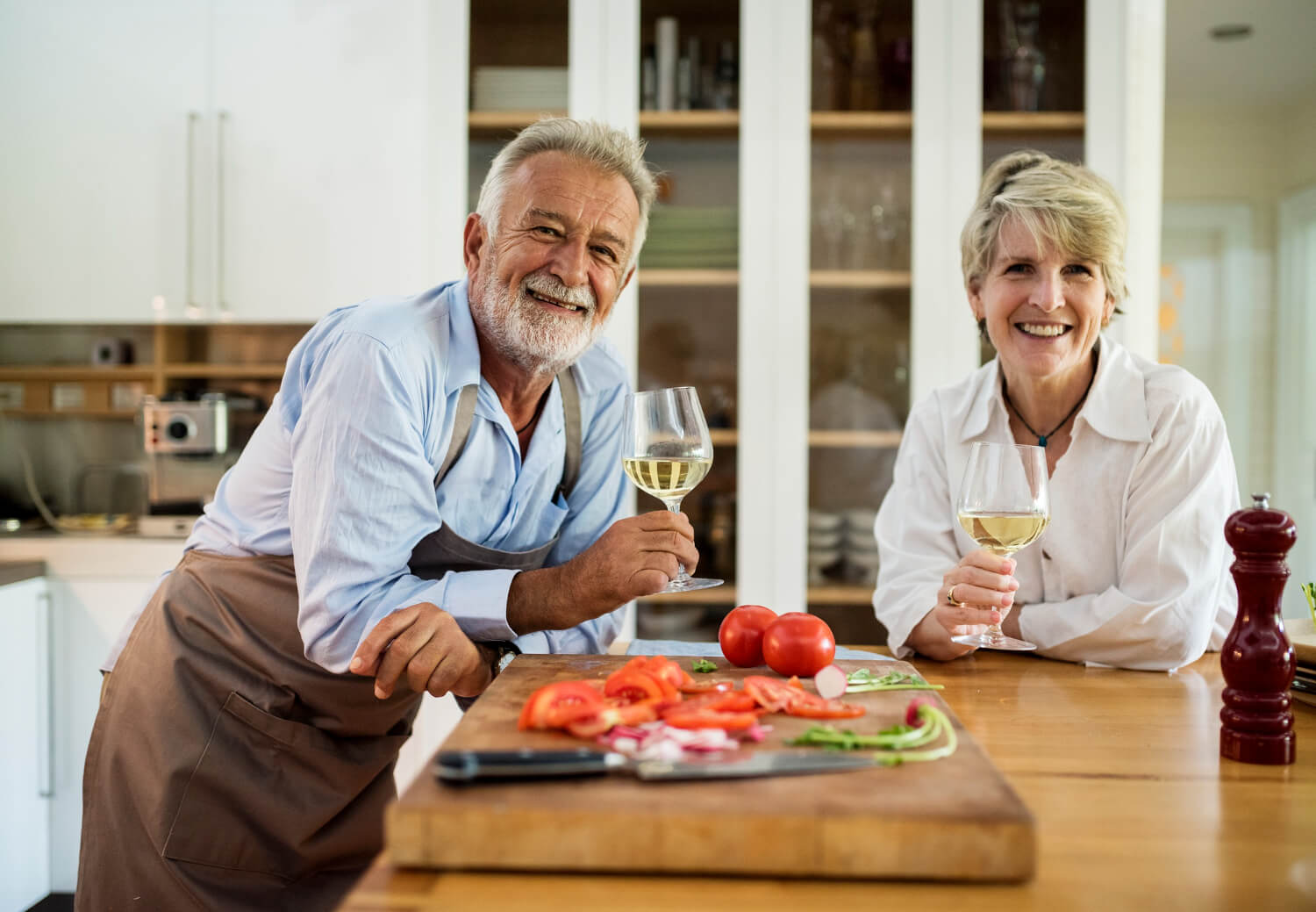 Casal sorrindo na cozinha com tomates. Mostra a alimentação após implante dentário na Perrella Odontologia em São Caetano do Sul.