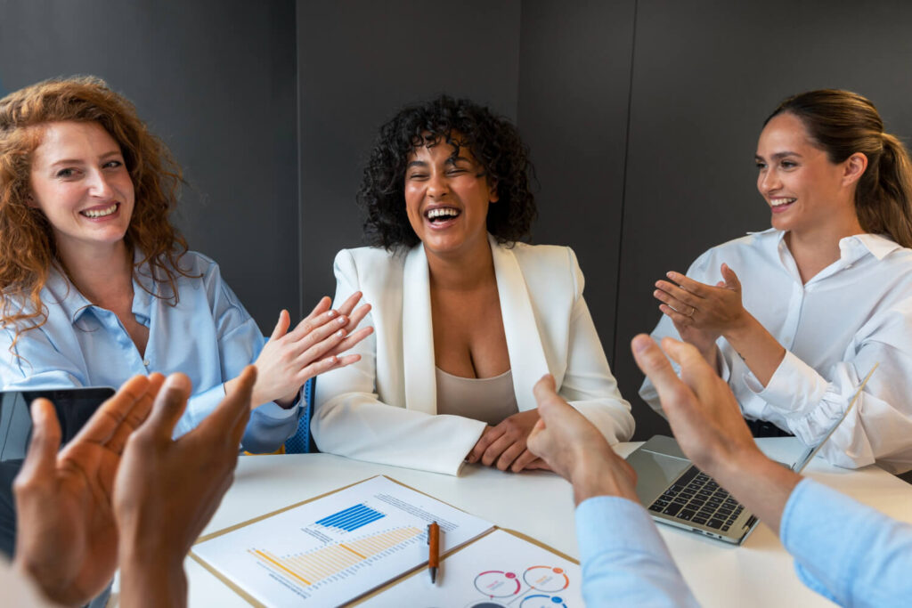 Mulheres em reunião corporativa sorrindo e aplaudindo, destacando a discrição e dicção com Invisalign na Clínica Perrella em São Caetano do Sul.