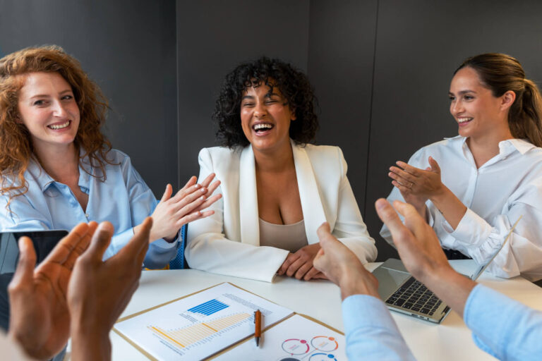 Mulheres em reunião corporativa sorrindo e aplaudindo, destacando a discrição e dicção com Invisalign na Clínica Perrella em São Caetano do Sul.