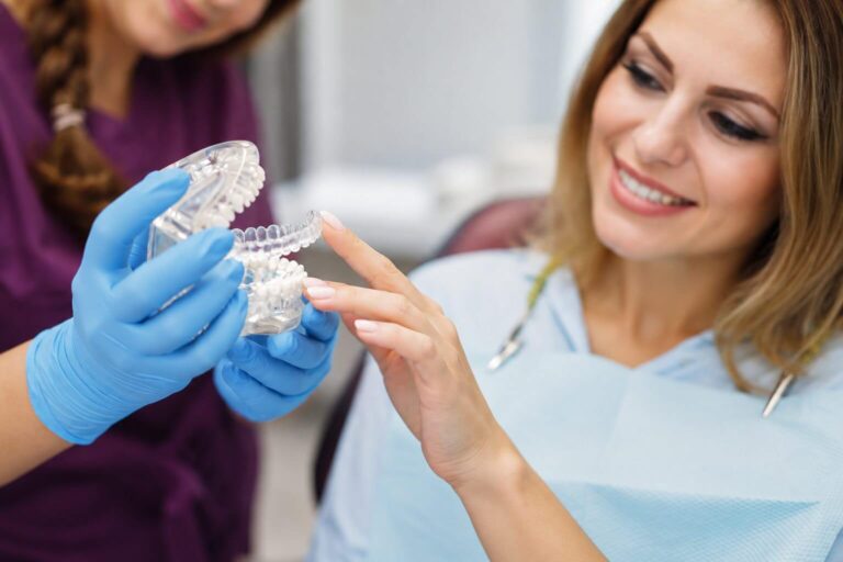 Dentista da Perrella Odontologia em São Caetano do Sul demonstra um alinhador transparente Invisalign em modelo para paciente sorrindo.