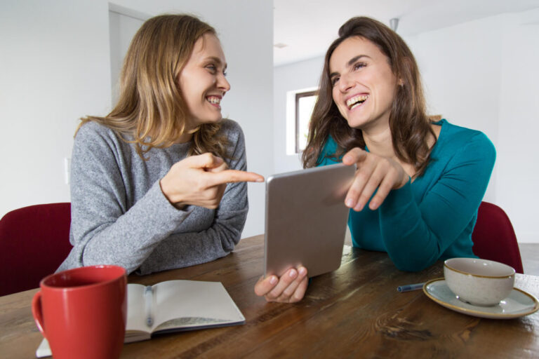 Duas amigas sorrindo e olhando um tablet sobre a mesa, conferindo o tempo de tratamento Invisalign na clínica em São Caetano do Sul.